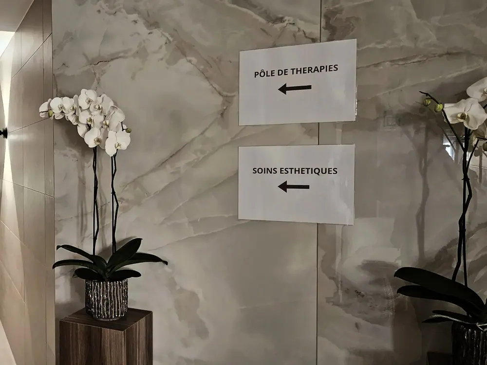Couloir de marbre clair avec des orchidées et les panneaux « Pôle de thérapies » et « Soins esthétiques »