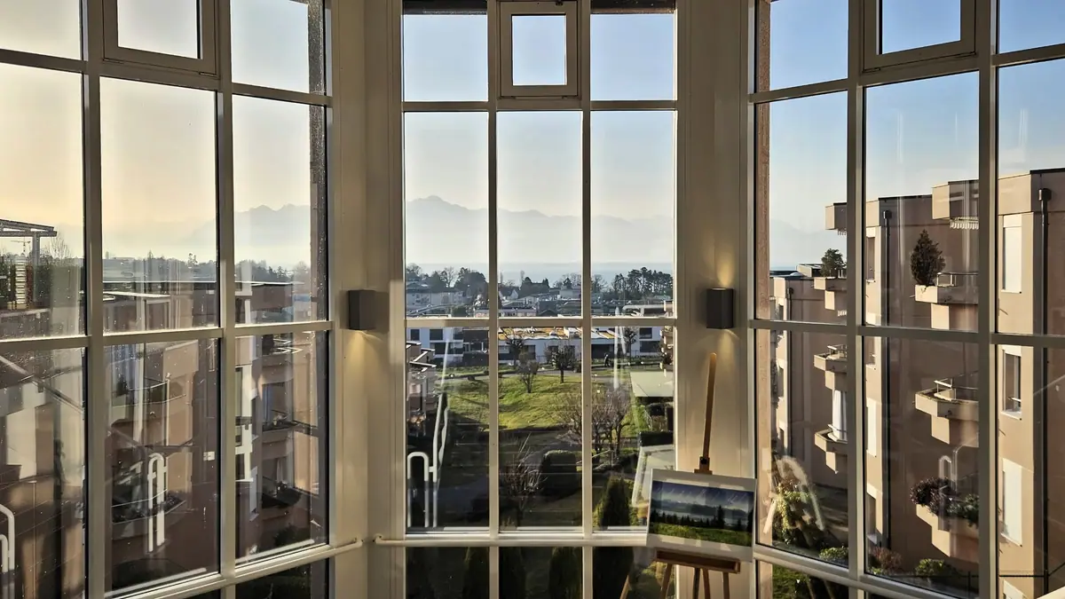 Vue sur le Léman et les Alpes depuis une grande fenêtre du Domaine
